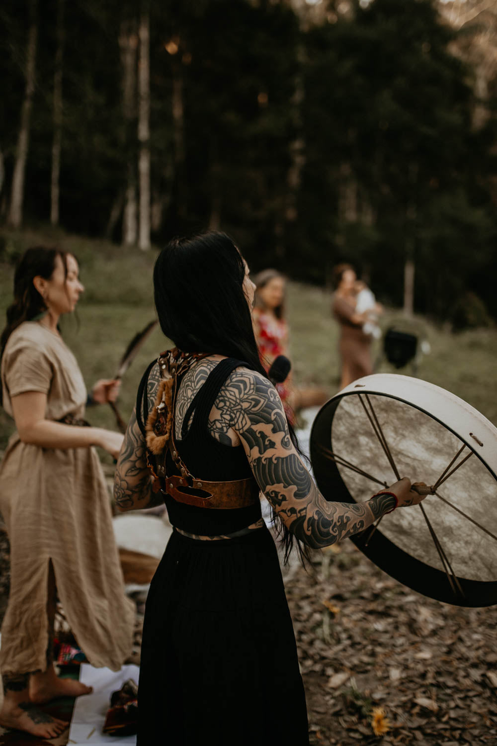 Woman with tattoos holding a medicine drum in a forest setting