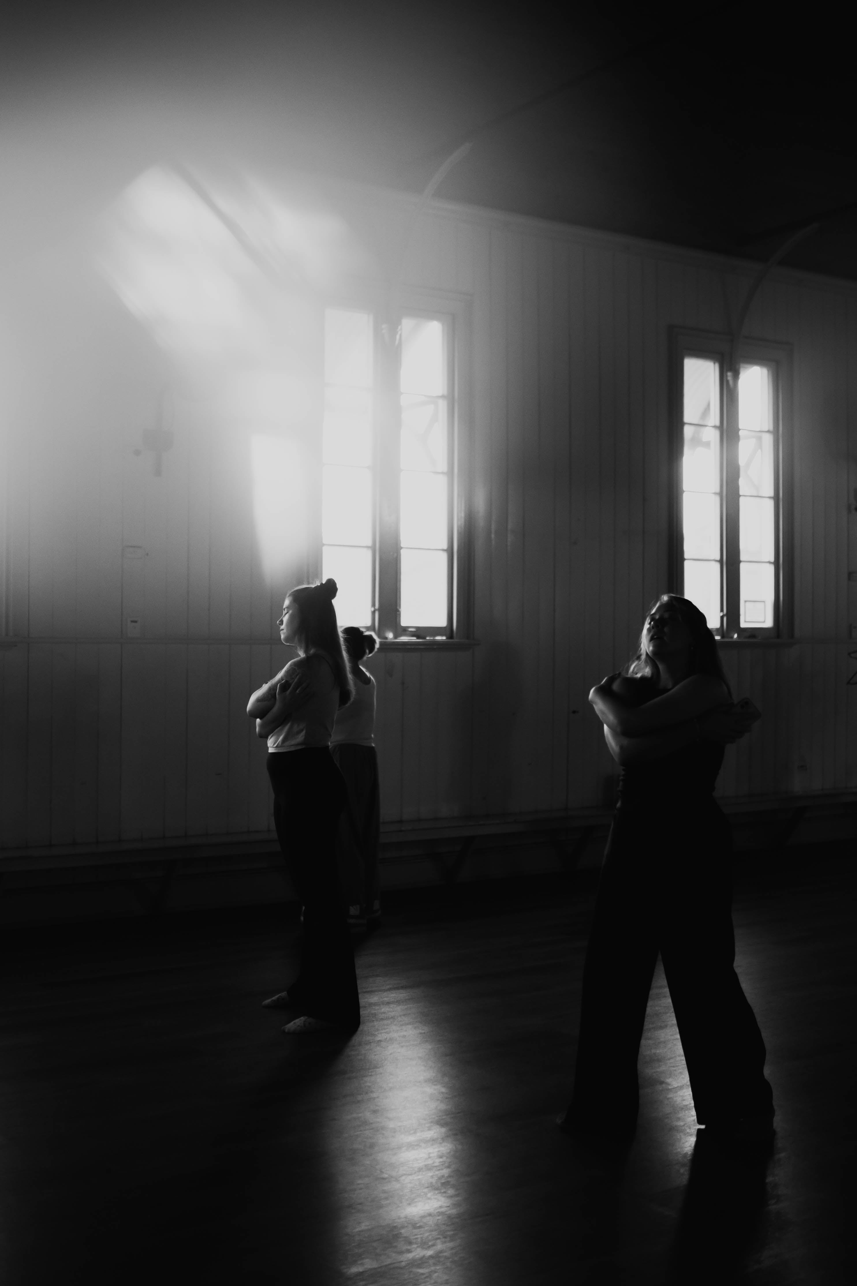 Two people standing in a dimly lit room with light streaming through windows.